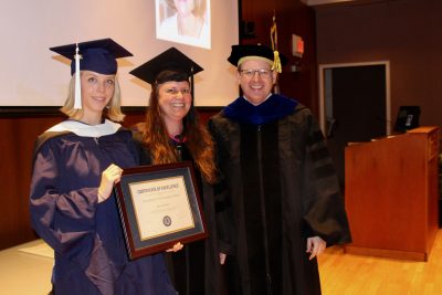Susan Bartlett Outstanding SLP Graduate Student, Anna Barnes holding her award on stage with Professor Spaulding and Dr. Houston. 